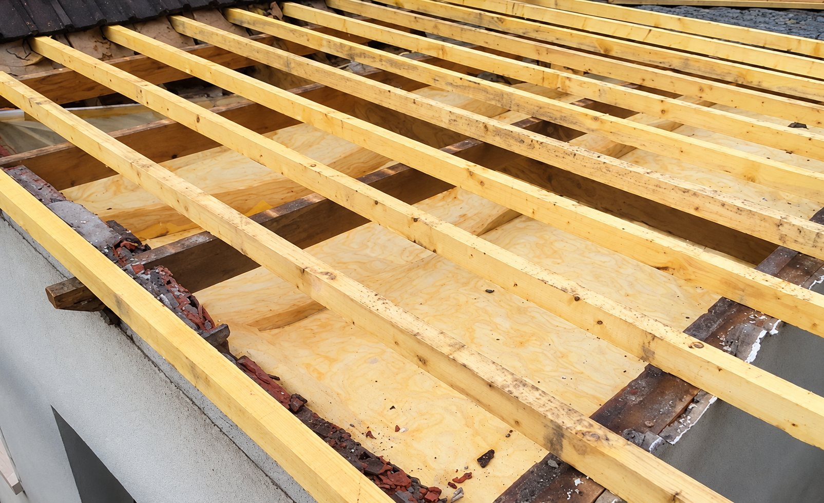 Vue d'une toiture en cours de rénovation avec des liteaux en bois posés sur un isolant jaune, au-dessus d'un mur enduit.
